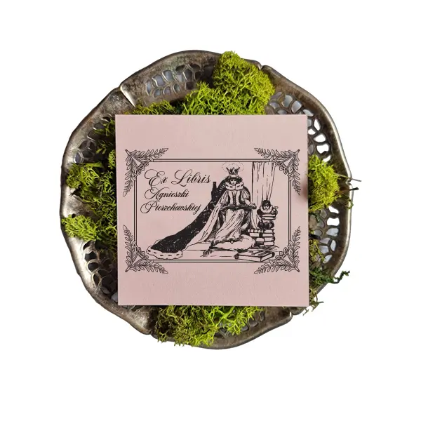 Pieczątka-ex-libris-do-książek-Królowa.jpg: Pieczątka ex libris do książek Królowa z imieniem Agnieszki Pierzchowskiej odbita na pudroworóżowym papierze w ozdobnej misie z zielonym mchem.