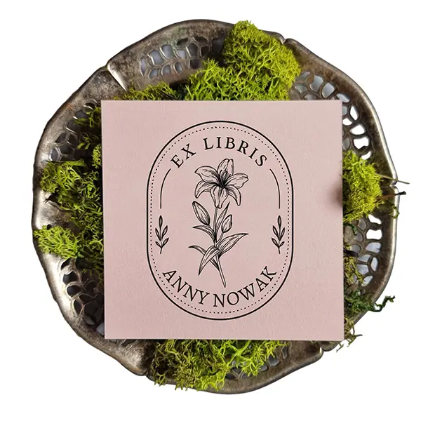 Personalizowany stempel do książek z lilią, wykonany z drewna bukowego, obok otwartej książki w domowej bibliotece.