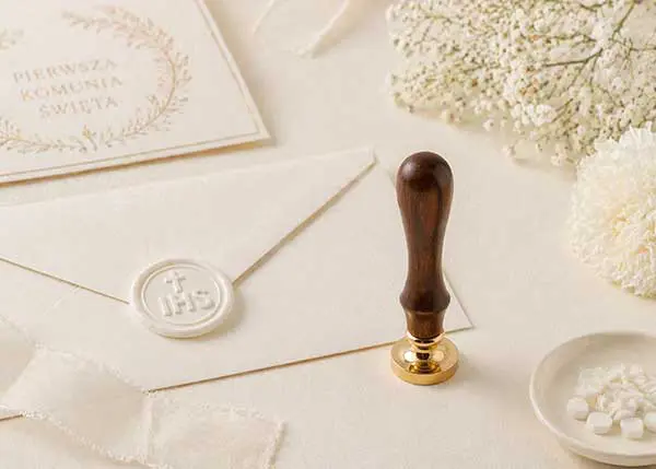 Odbicie w białym laku z monogramem IHS na eleganckiej kopercie w kolorze złamanej bieli.